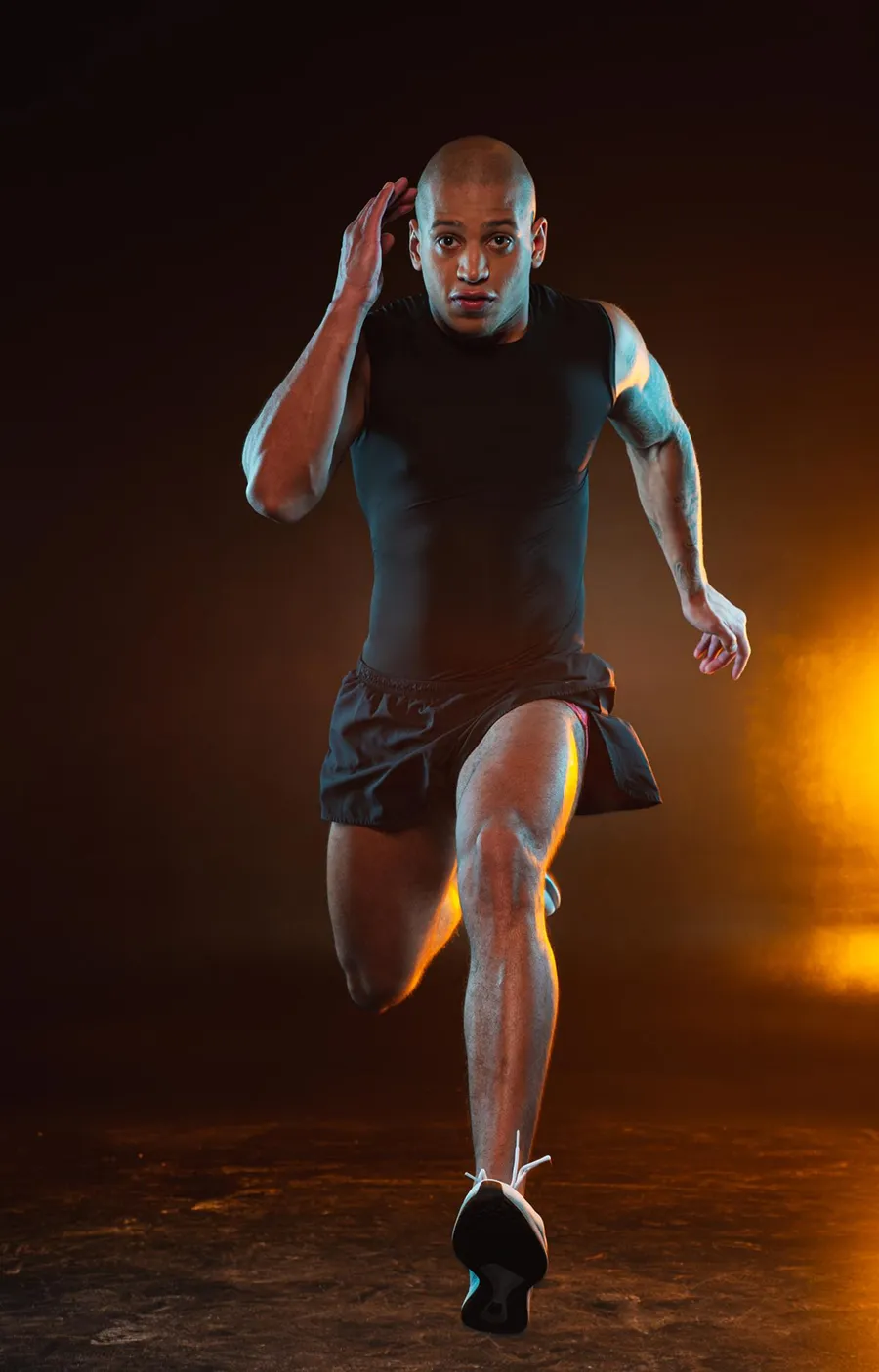 Older athlete sprinting on track under orange spotlight.